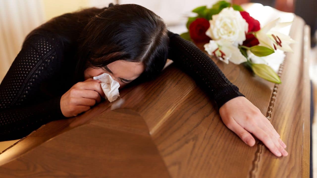 people and mourning concept - crying woman with coffin at funeral in church