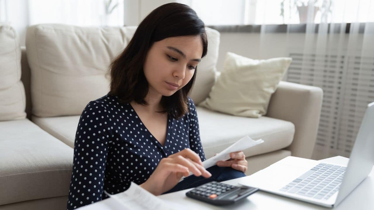 millennial vietnamese female engaged in home banking using calculator and laptop. Controlling Another's Finances