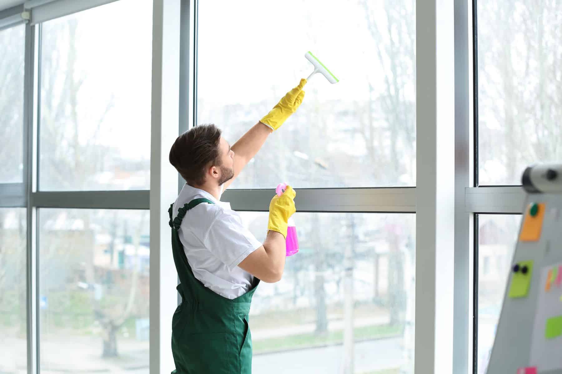 Male janitor cleaning window in office