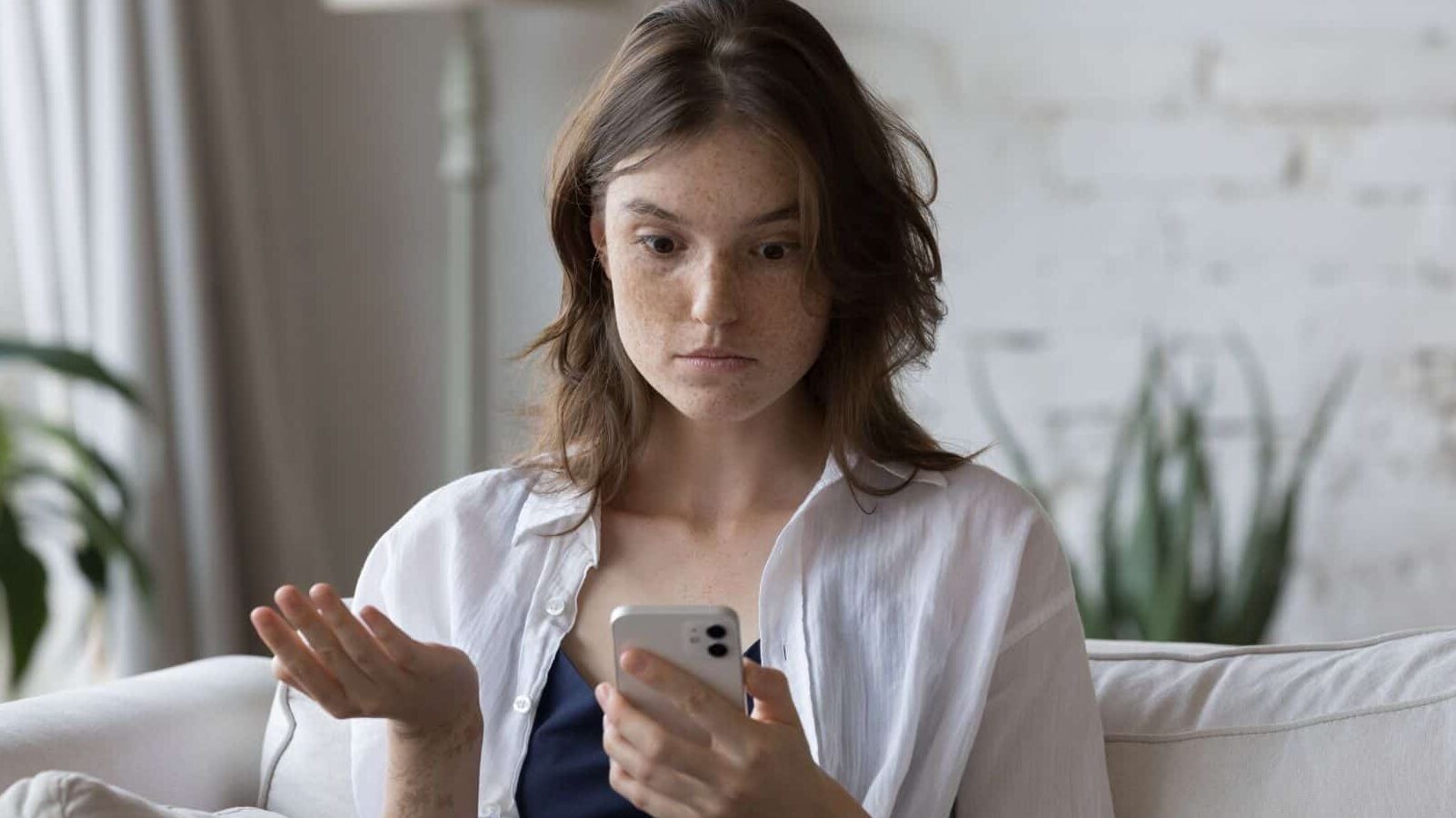 Shocked concerned cellphone user girl staring at screen, looking at smartphone screen, finding problems with online app, poor connection, Internet service, getting surprising bad news