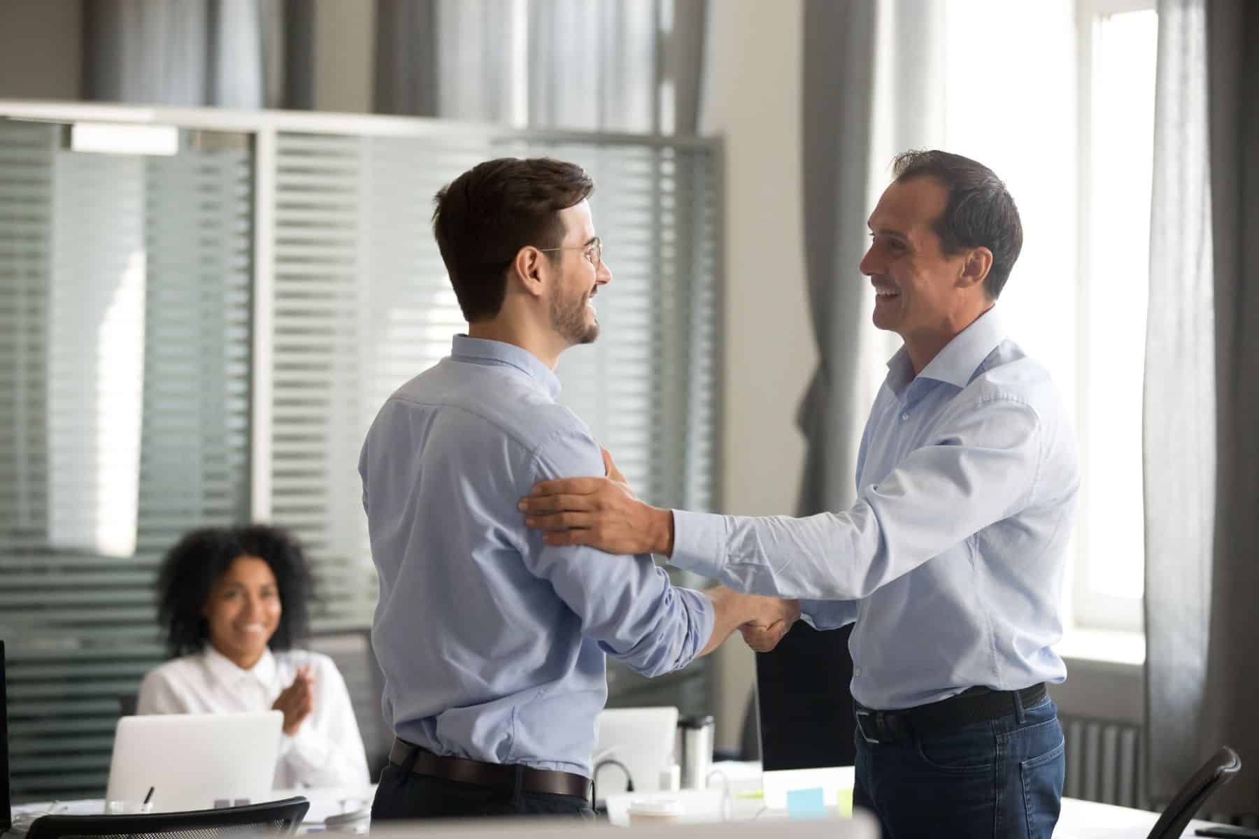 Smiling middle-aged ceo promoting motivating worker shaking hands congratulating with achievement promising respect bonus thanking for good work