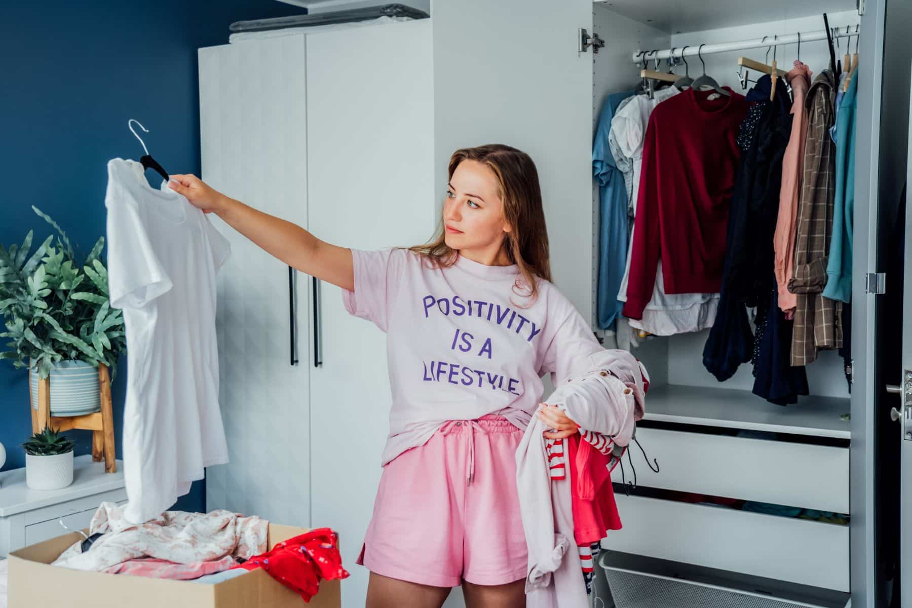 Woman selecting clothes from her wardrobe for donating to a Charity shop. Decluttering, Sorting clothes and Cleaning Up.