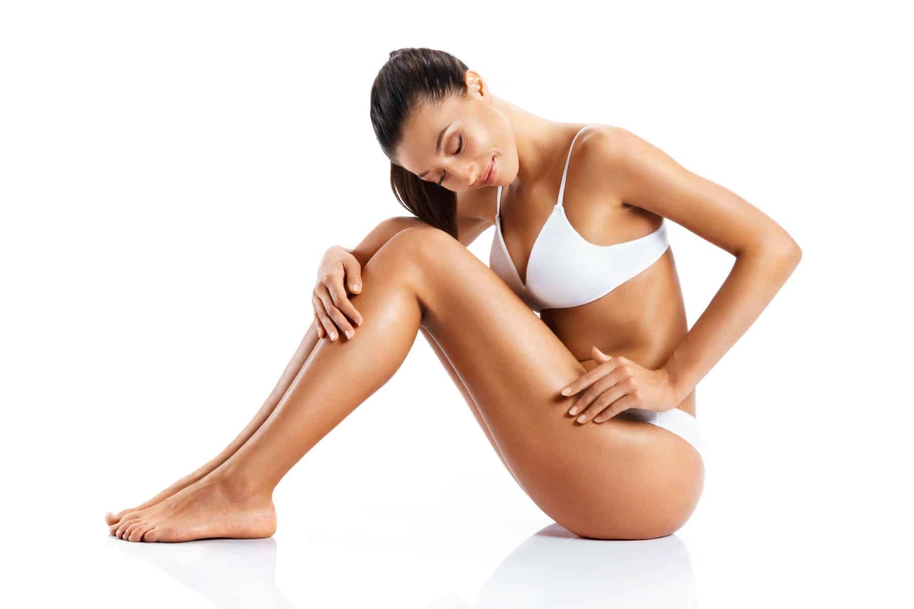 Young girl with perfect body touching her leg sitting on white background. Beauty & Skin care concept